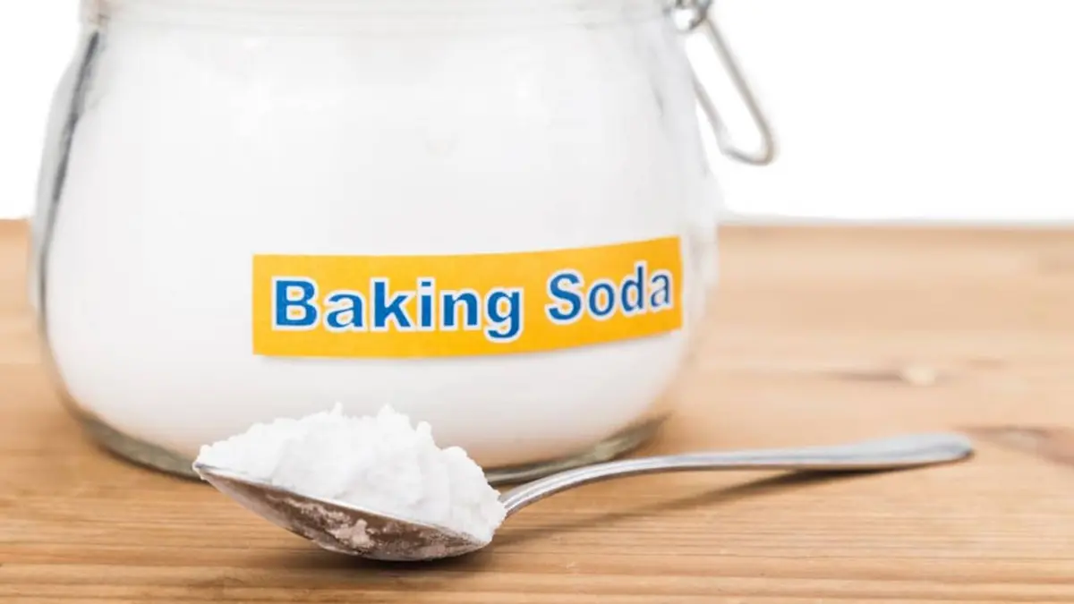 Applying baking soda paste to remove grease from a stainless steel countertop.