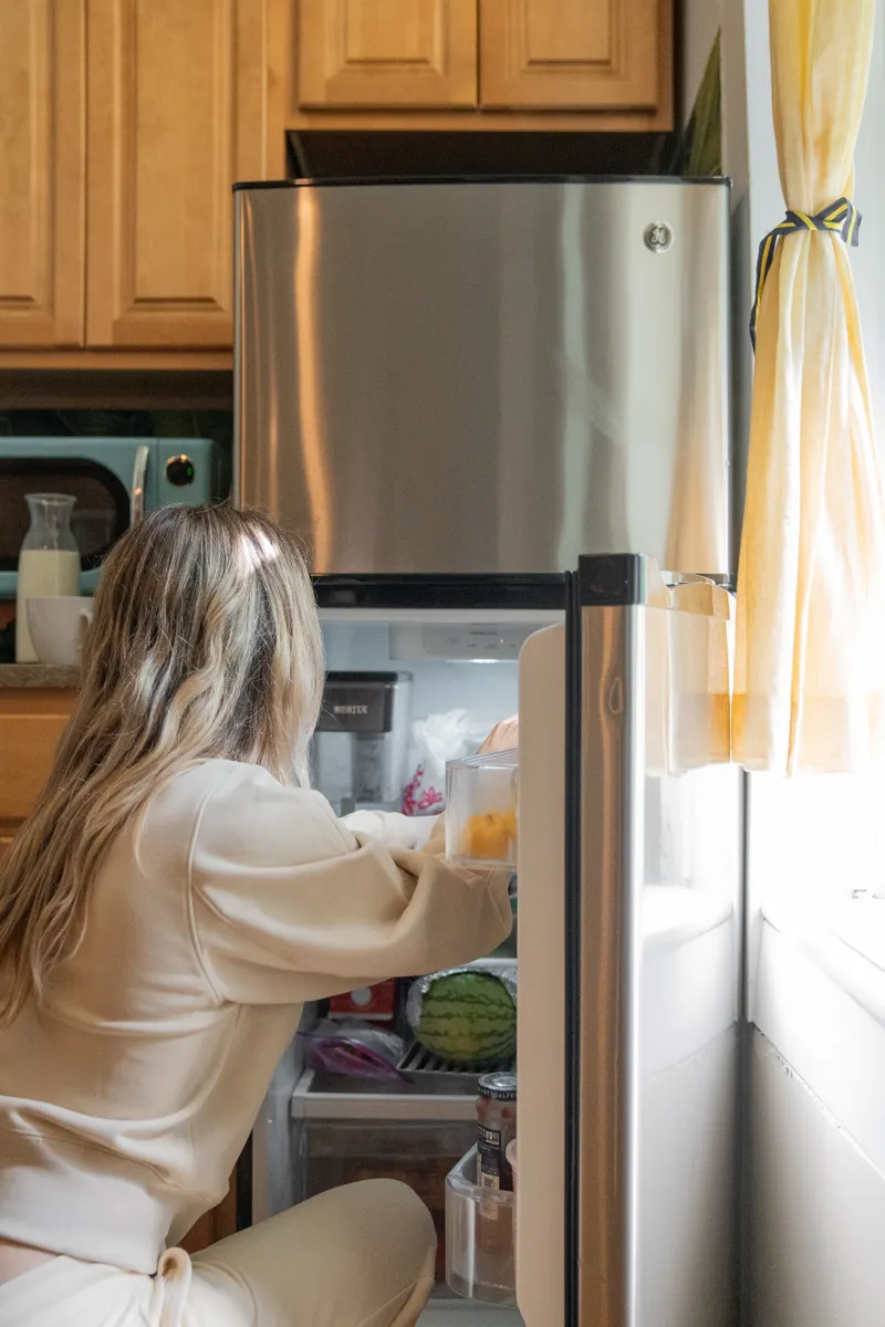 A person checking the drip pan location at the bottom of a refrigerator.