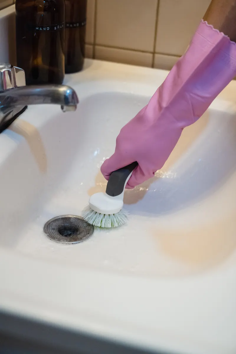 A bottle of chemical drain cleaner sitting next to a stainless steel kitchen sink.