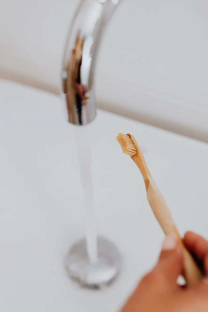 Soft-bristle toothbrush cleaning grime from the grooves of a kitchen faucet handle.