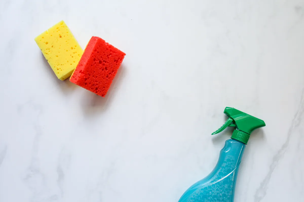 A kitchen sponge next to a spray bottle, illustrating how cleaning products affect tool longevity.