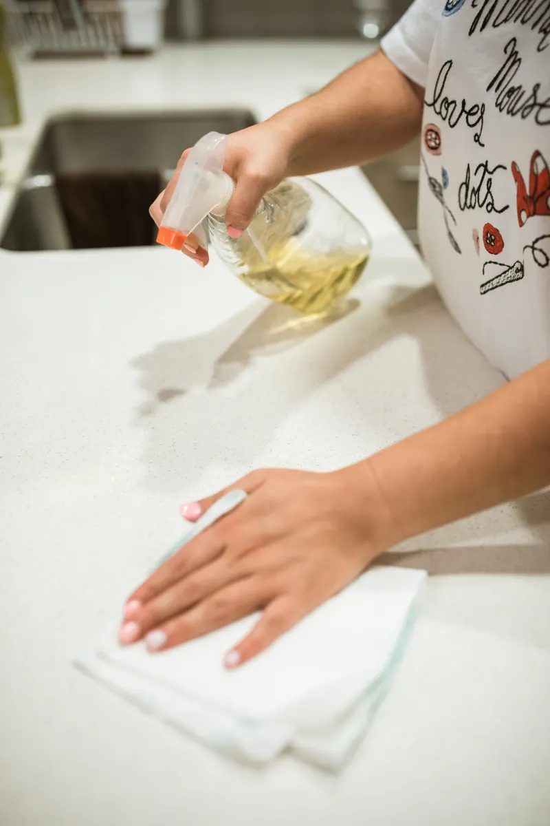 Wiping sticky residue from a kitchen countertop using a damp cloth and dish soap.