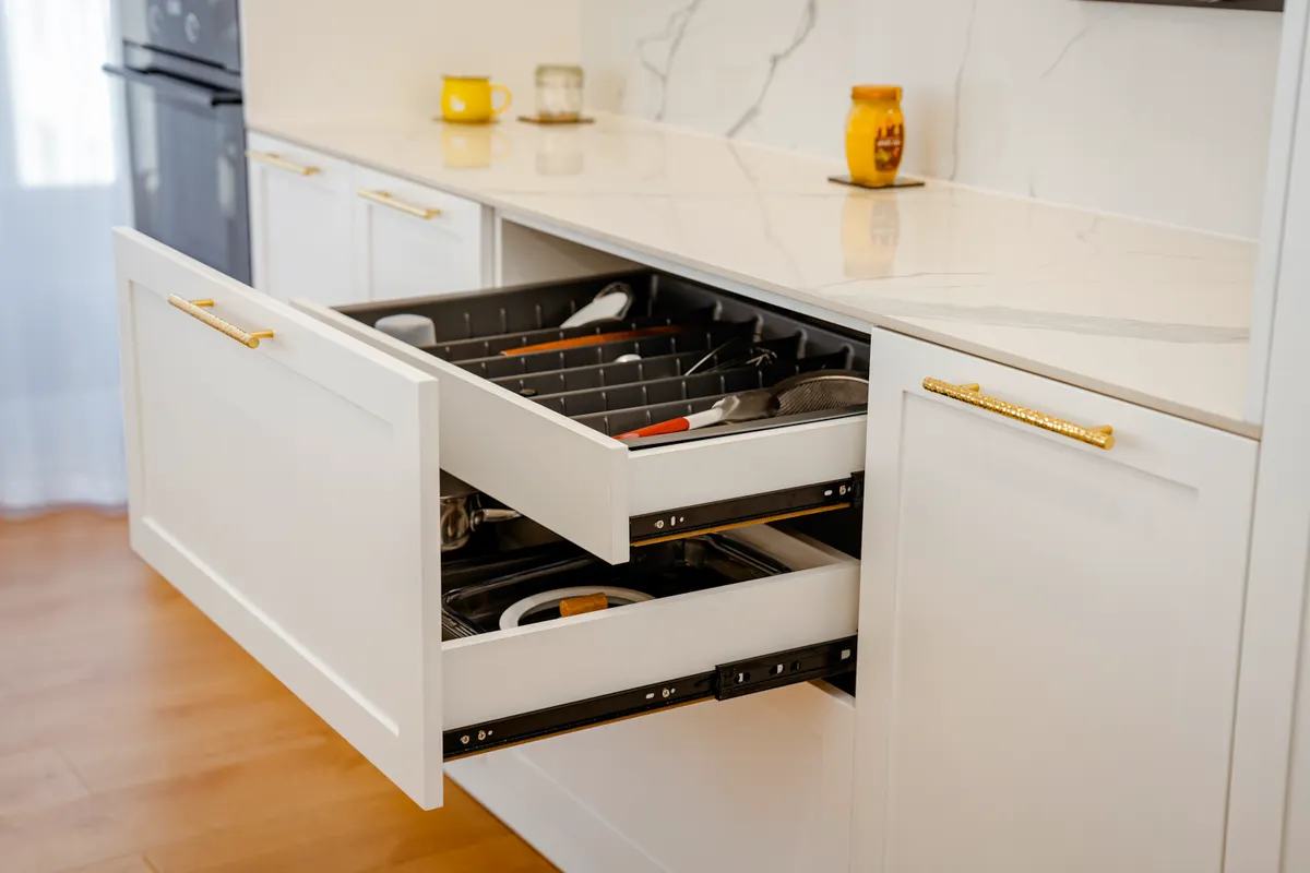 A deep kitchen drawer containing pots, pans, and baking sheets during a routine cleaning process.