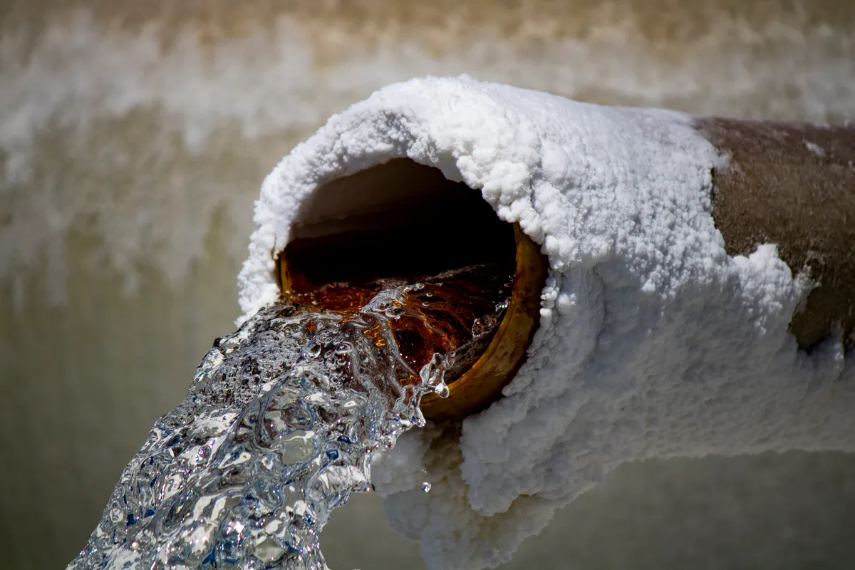 Close-up of a refrigerator water dispenser nozzle with slight mineral deposits around the opening.