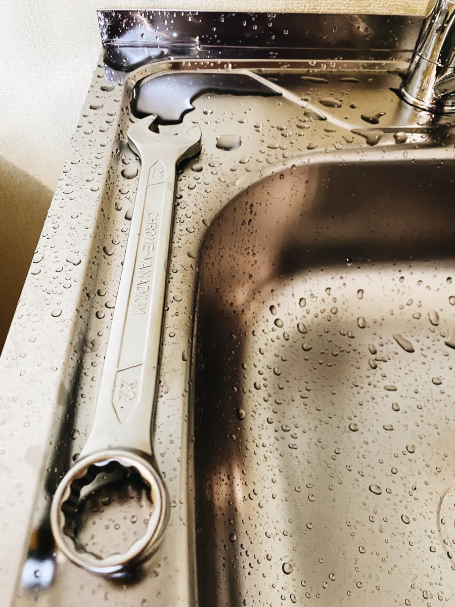 Inspecting a leaking pipe under the kitchen sink to find the true source of bad odors.