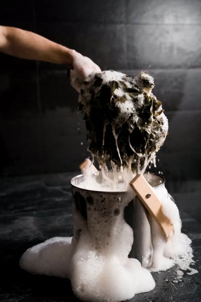 A metal mesh grease filter soaking in a basin of hot soapy water.