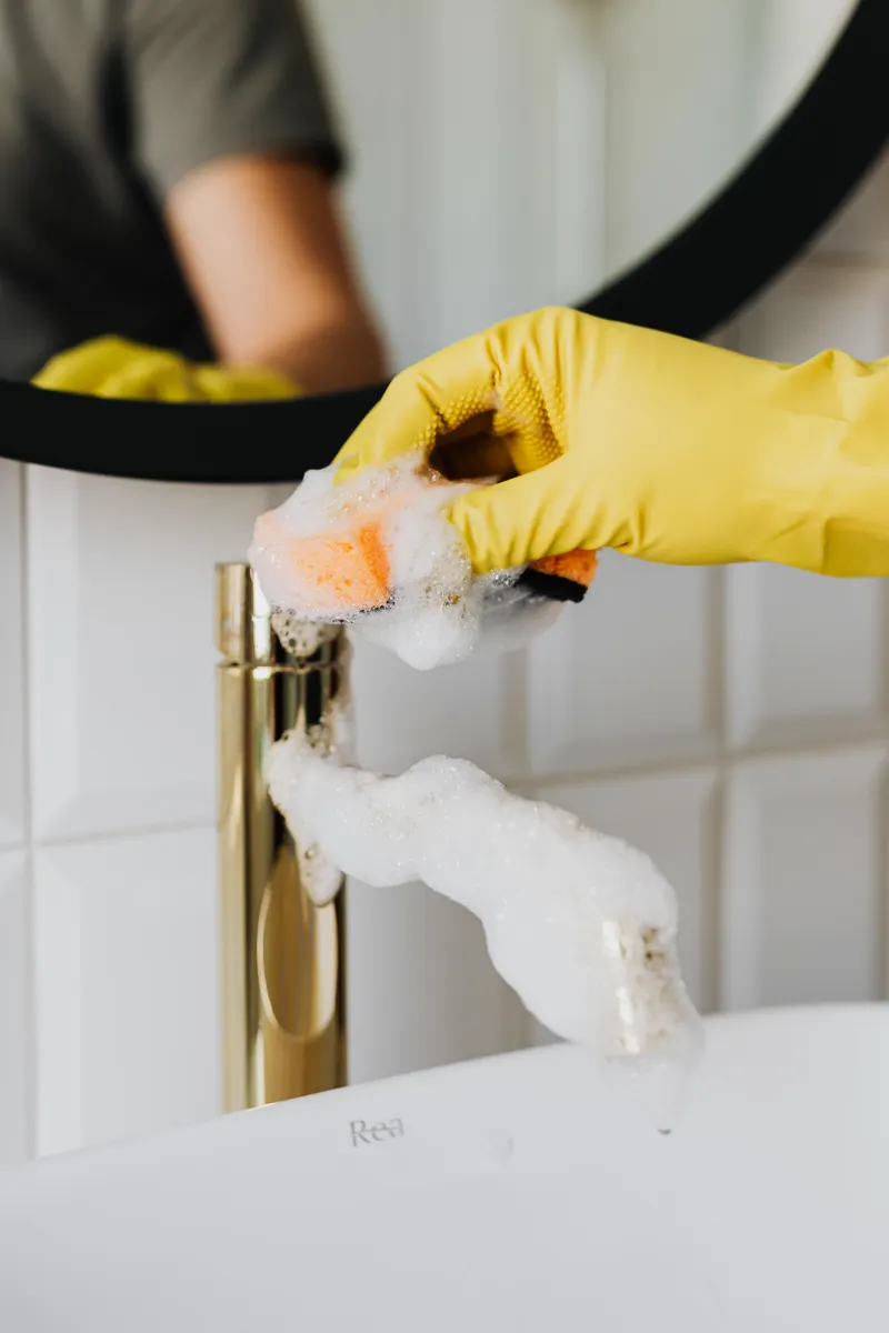 Cleaning supplies including mild dish soap and a soft microfiber cloth near a faucet.