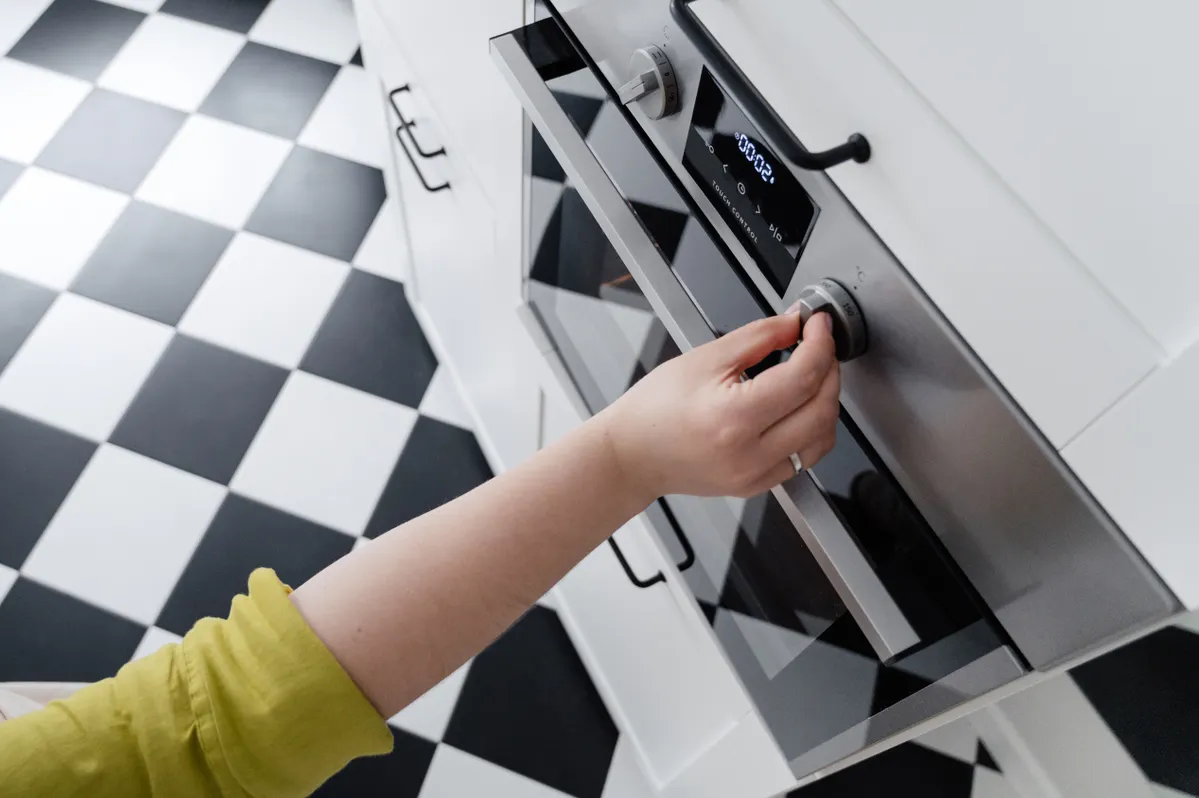Wiping down an oven control panel and removable knobs with a damp cloth.