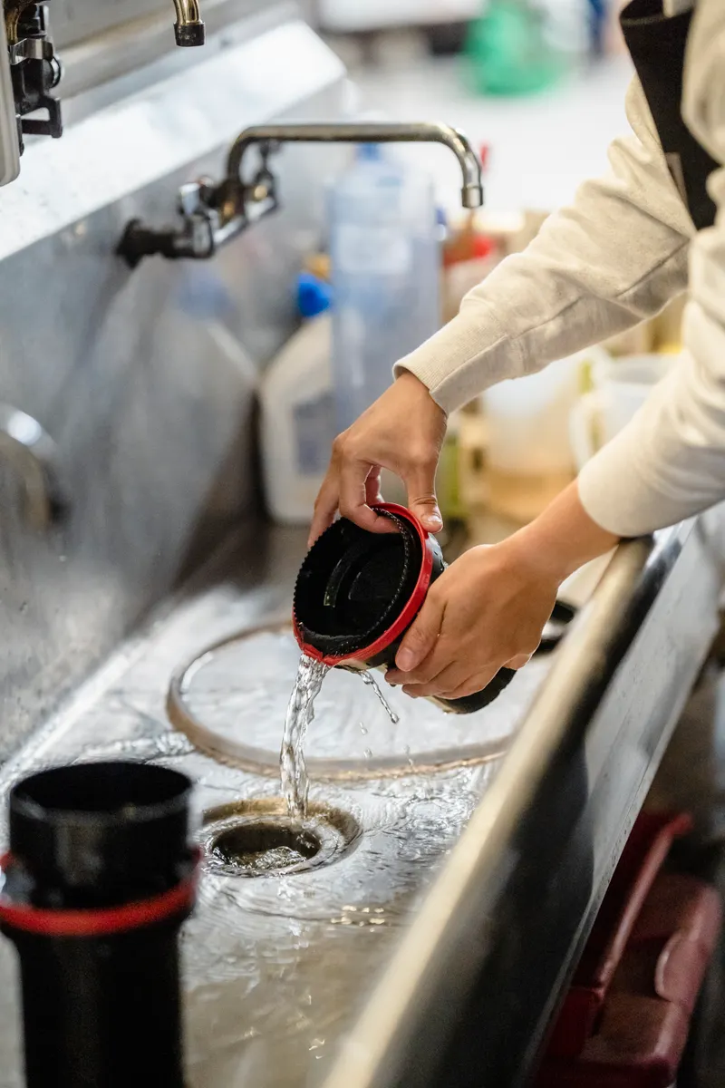 Hands carefully reattaching a clean sink stopper into the dry kitchen drain area.