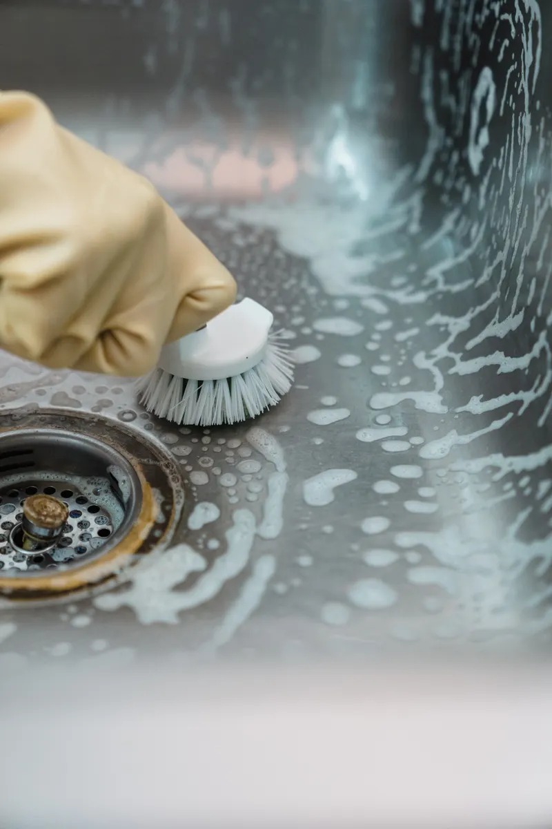Wiping mineral spots off stainless steel basin surface using a vinegar solution cloth.