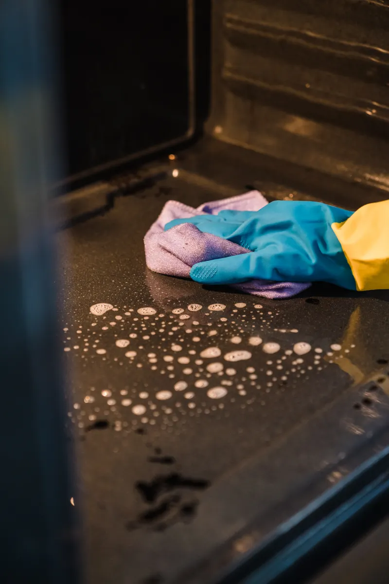 Applying baking soda paste to remove heavy burnt residue inside an oven interior.