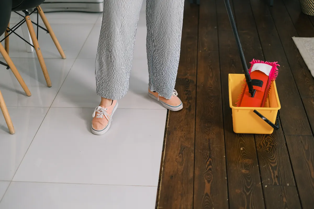 A person rinsing a mop bucket while following proper floor cleaning steps.