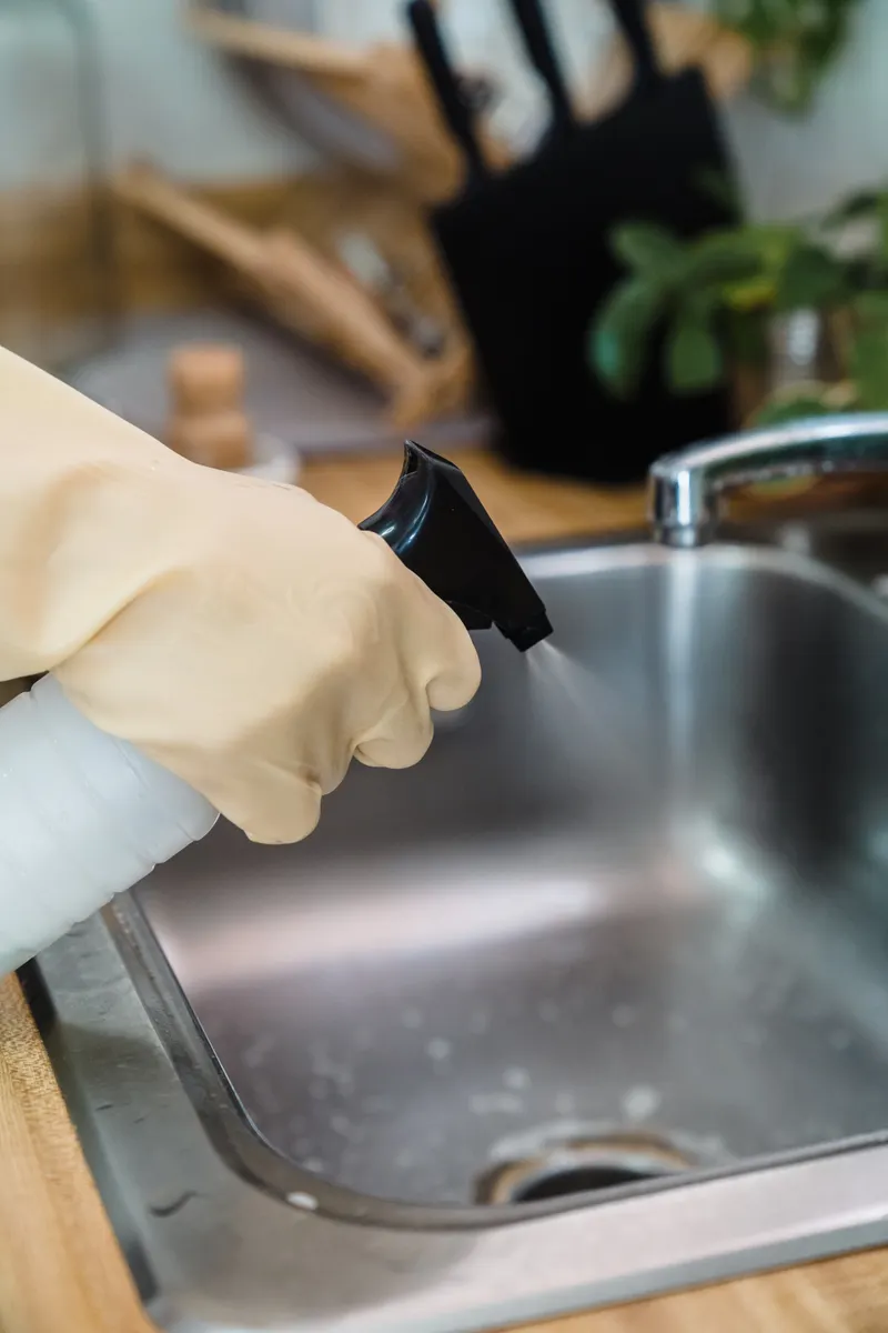 A spray bottle with a vinegar solution next to a clean kitchen sink