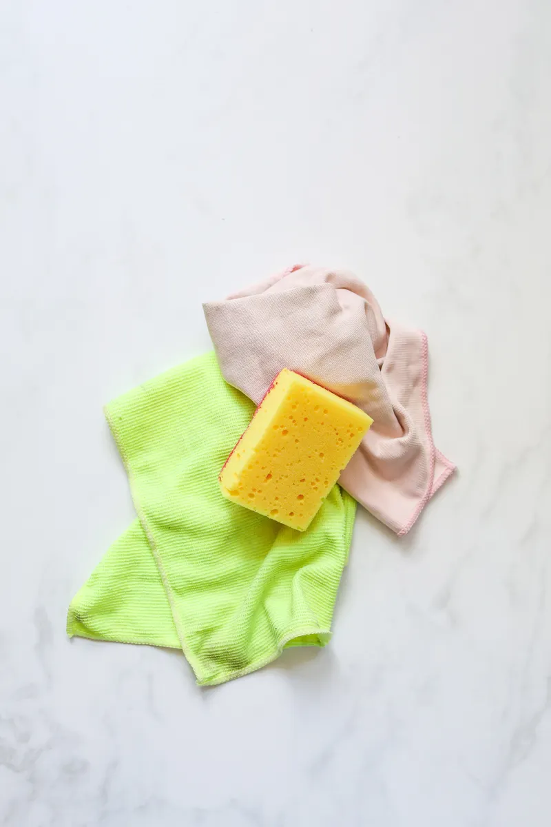 A soft microfiber cloth and a mild pH neutral cleaner resting on a white marble counter.