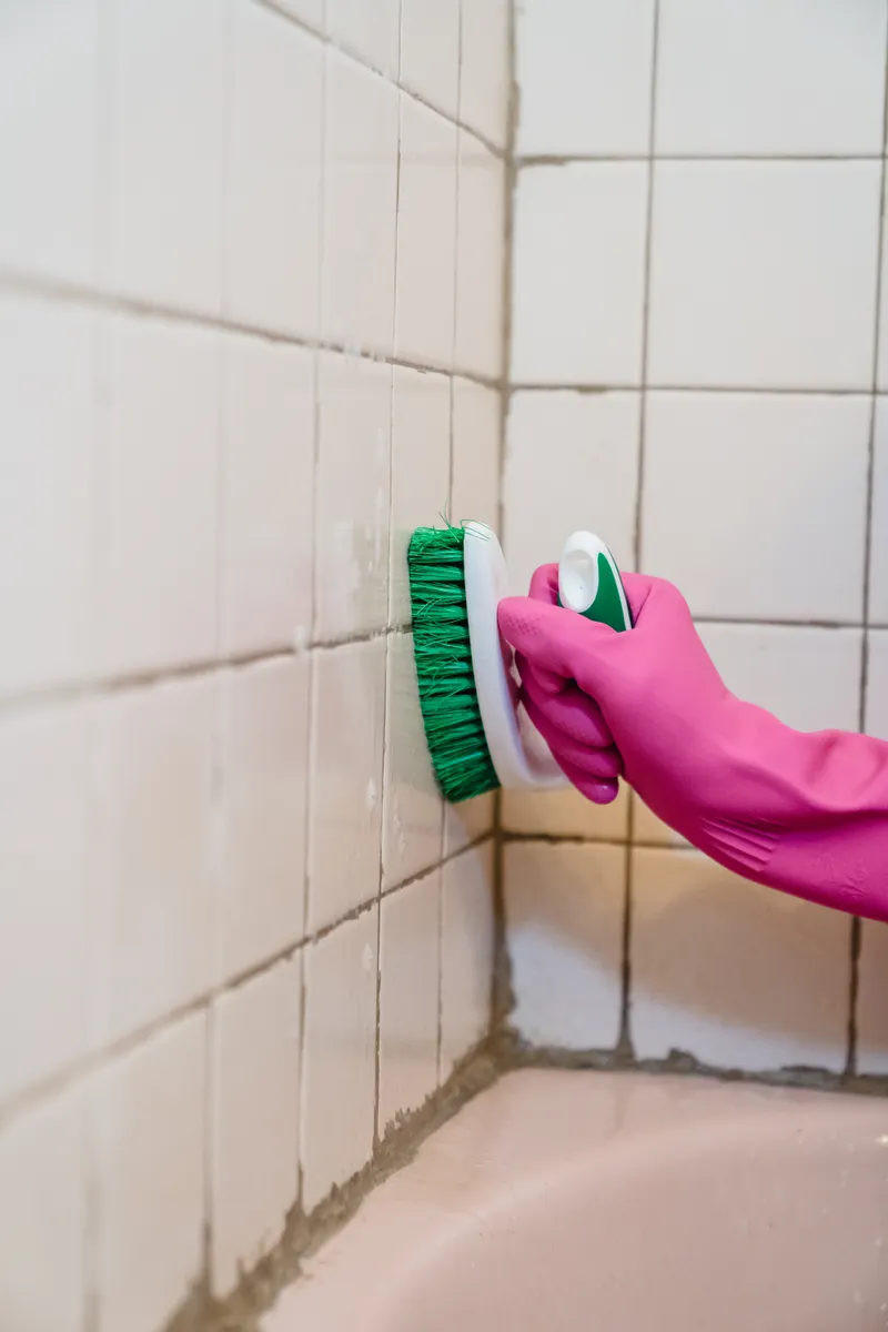 Soft-bristle brush scrubbing grease buildup from tile backsplash grout lines