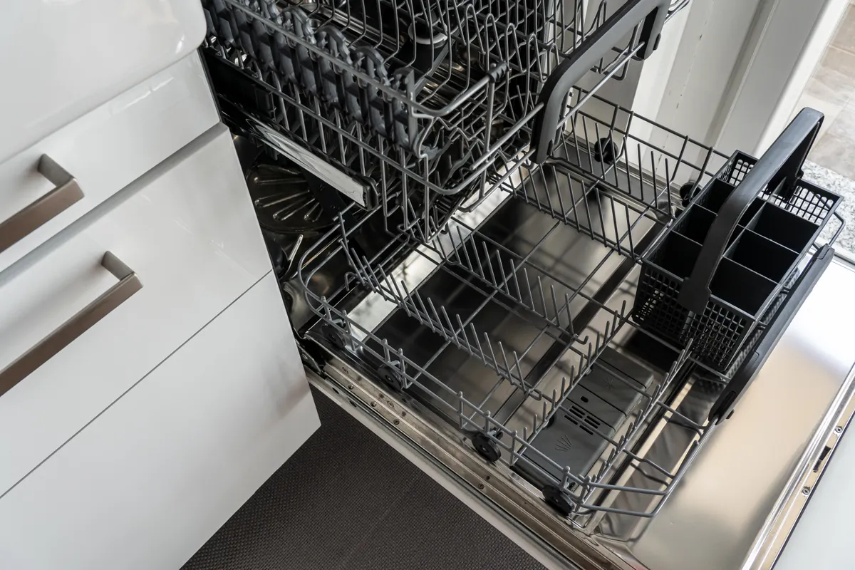 Pouring white vinegar into a container on the dishwasher top rack for a cleaning cycle.
