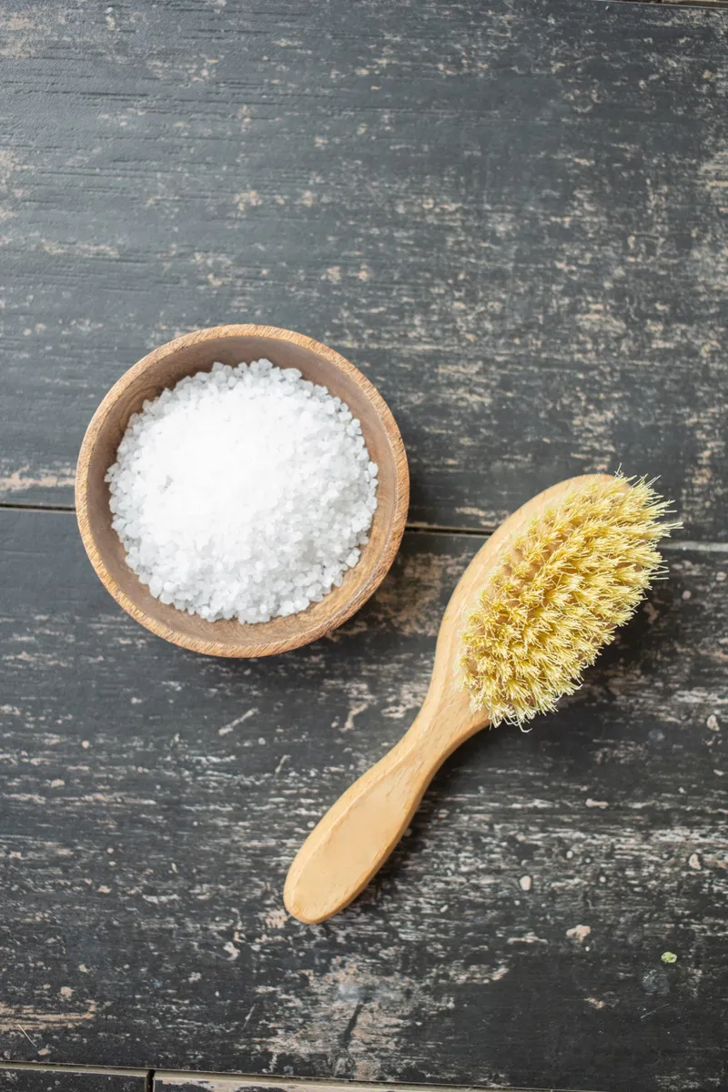 Applying baking soda paste with a soft brush to remove mineral buildup inside the sink.